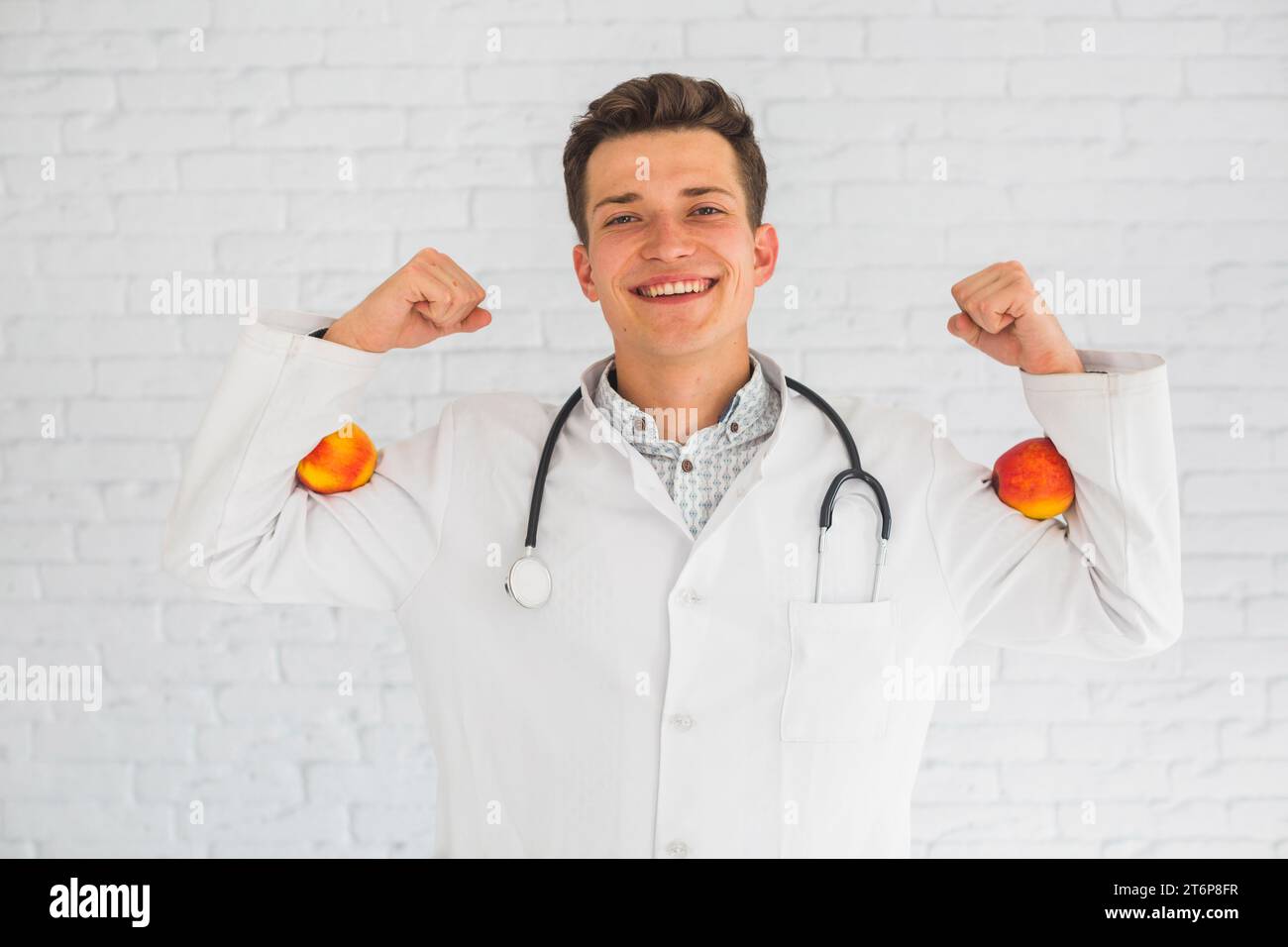 Ein männlicher Arzt beugt ihre Hände und hält rote Äpfel im Bizeps Stockfoto