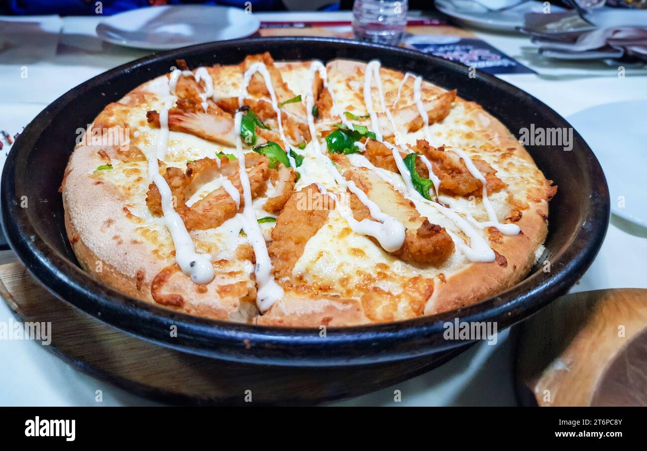 Pizza mit Alfredo-Sauce, serviert auf schwarzem Teller auf weißem Tisch mit Leuten herum Stockfoto