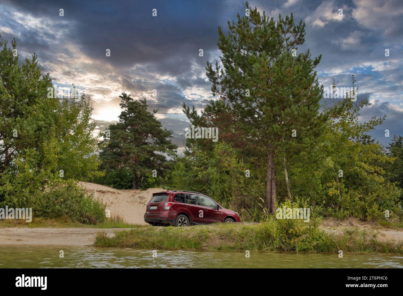Roter SUV-Wagen in einer Sandgrube im Wald am See. Stockfoto