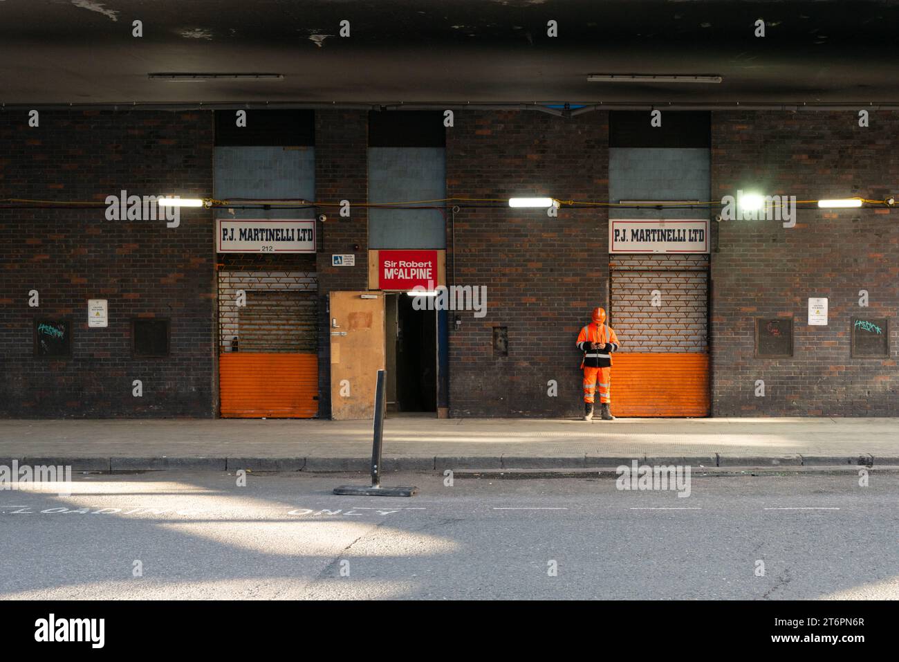 Ein Bauarbeiter steht vor einem Gebäude in Smithfield Market, London, neben einem Schild für Sir Robert McAlpine, ein britisches Bauunternehmen Stockfoto