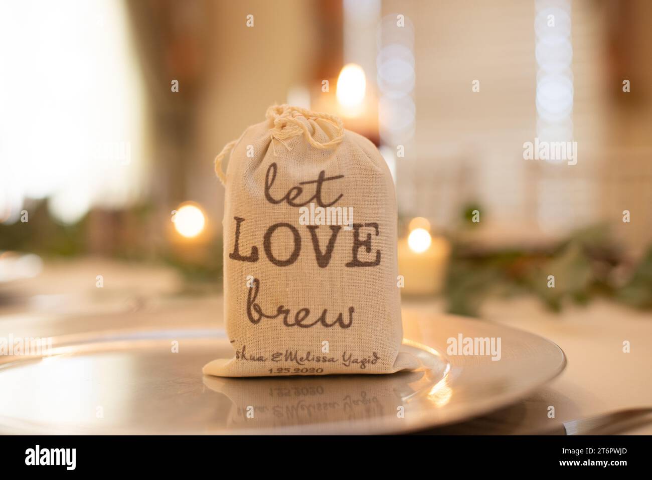 Leinentasche mit der Aufschrift „Let Love Brew“ Hochzeitsmitte gefüllt mit Cofee Grinds auf dem Esstisch Stockfoto