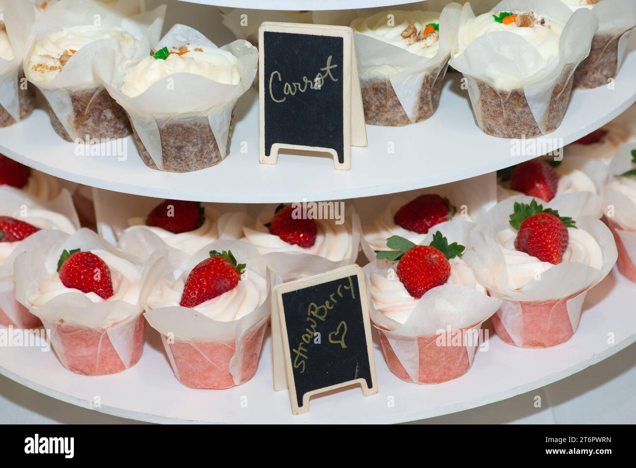 Erdbeeren- und Karotten-Cupcakes auf Kuchenständer mit Tafelschildern Stockfoto