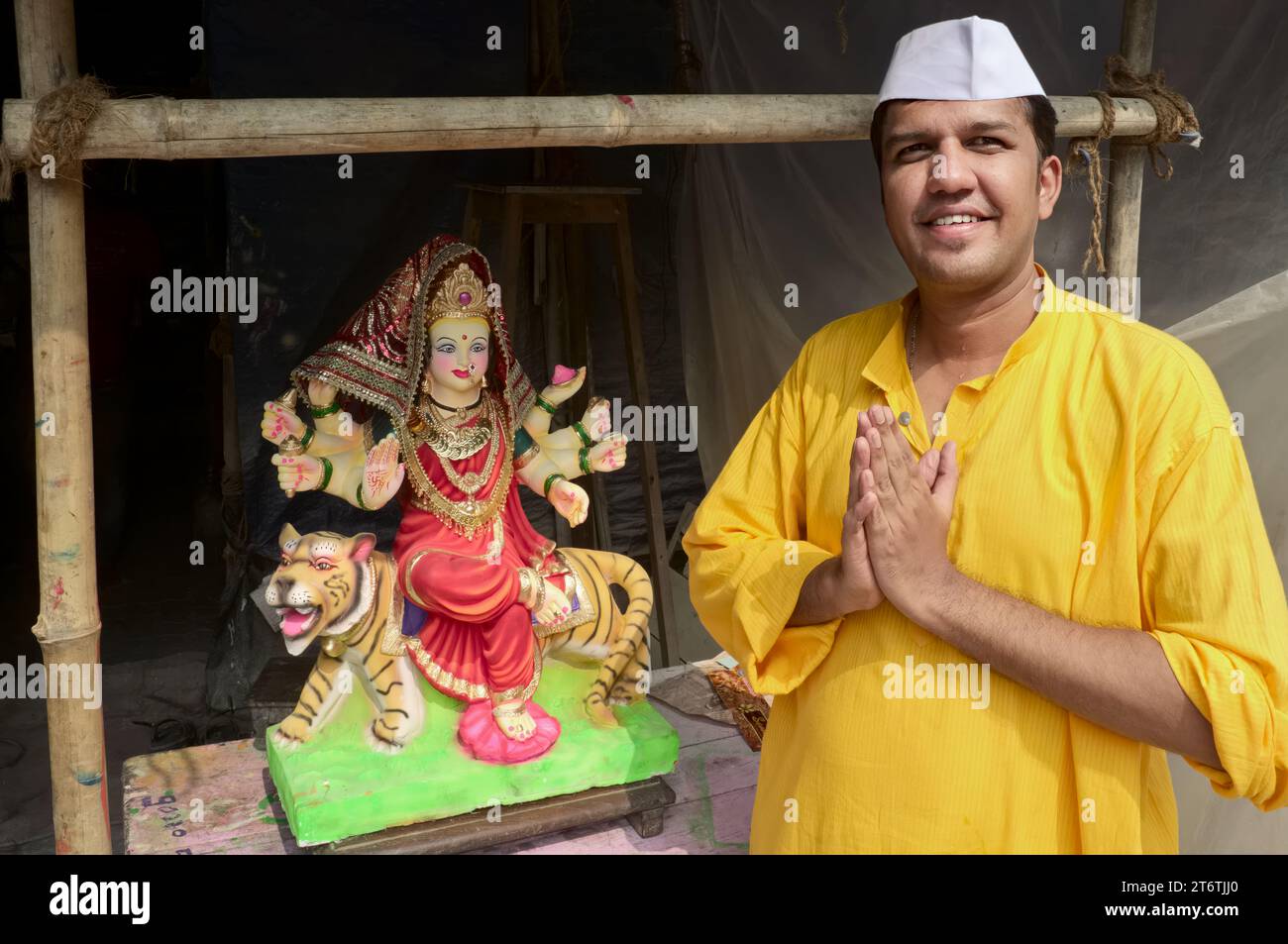 Neben einer Figur der hinduistischen Göttin Durga legt ein Mann seine Hände für den Trad zusammen. Indische Begrüßung; in einer Werkstatt für Hindu-Statuen, Mumbai, Indien Stockfoto