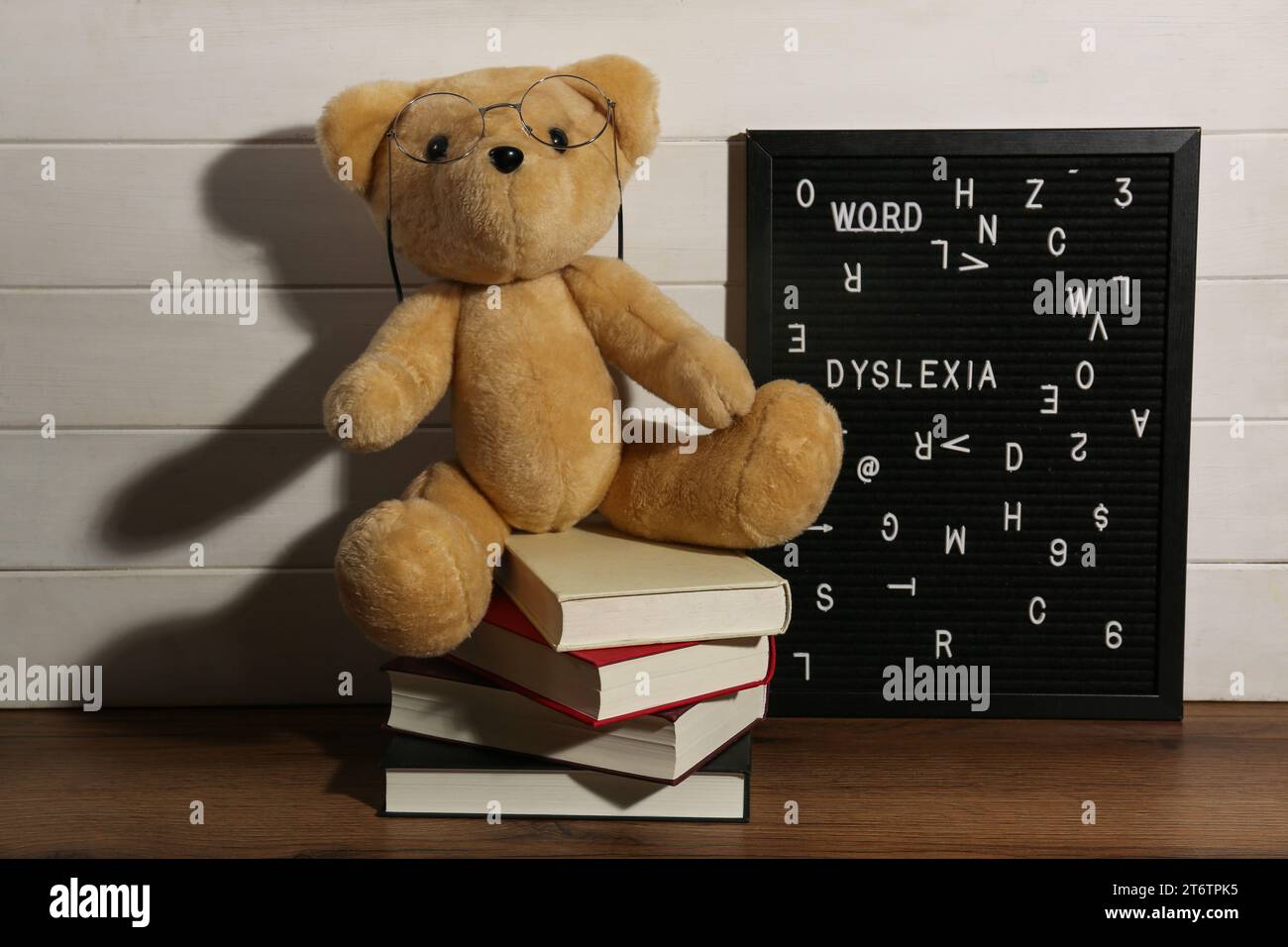 Schwarze Brieftafel mit dem Wort Dyslexia, Bücher und Teddybär auf Holztisch in der Nähe der weißen Wand Stockfoto
