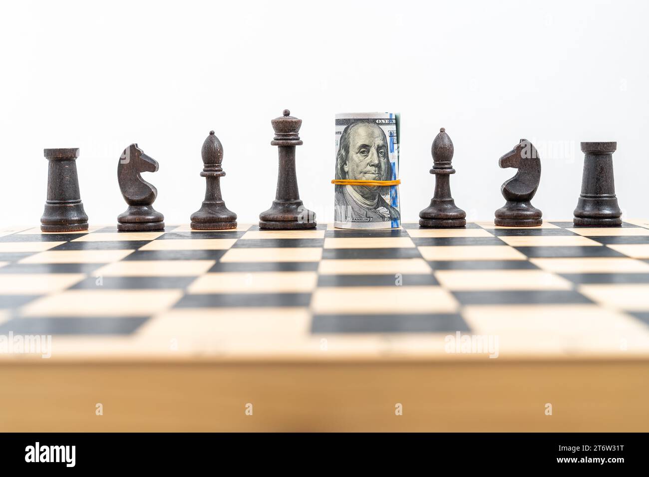 Schachbrett mit einer Reihe schwarzer Figuren, amerikanische Banknoten, die anstelle des schwarzen Königs gerollt und platziert wurden, zwei schwarze Türme, Ritter, Bischöfe, ein schwarzes Qu Stockfoto
