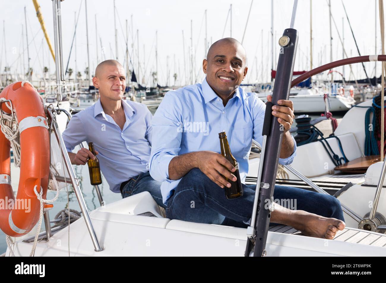 Zwei Männer in blauen Hemden, die sich auf einer Segelyacht im Hafen entspannen Stockfoto