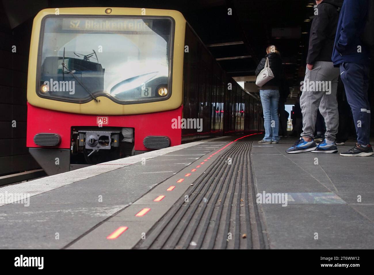 09.11.2023, Berlin, DE - Rot leuchtende Bahnsteigkante am S-Bahnhof Suedkreuz bei Einfahrt eines Zuges. Alltag, Aussen, Aussenaufnahme, Bahn, Bahnhof, Bahnstation, Bahnsteig, Bahnsteigkante, Bahnverkehr, befoerdern, Befoerderung, Berlin, deutsch, Deutschland, einfahren, Einfahrt, Europa, europaeisch, Froschperspektive, Gesellschaft, Herbst, Jahreszeit, LED-Leitsystem, LED-Leuchten, Leitsystem, leuchtend, Lichtssteuerung, Menschen, Nahverkehr, oeffentlicher Nahverkehr, oeffentlicher Personennahverkehr, OEPNV, Personen, Personenbeförderung, Personentransport, QF, Querformat, rot, S 2, S-Bahn, Stockfoto