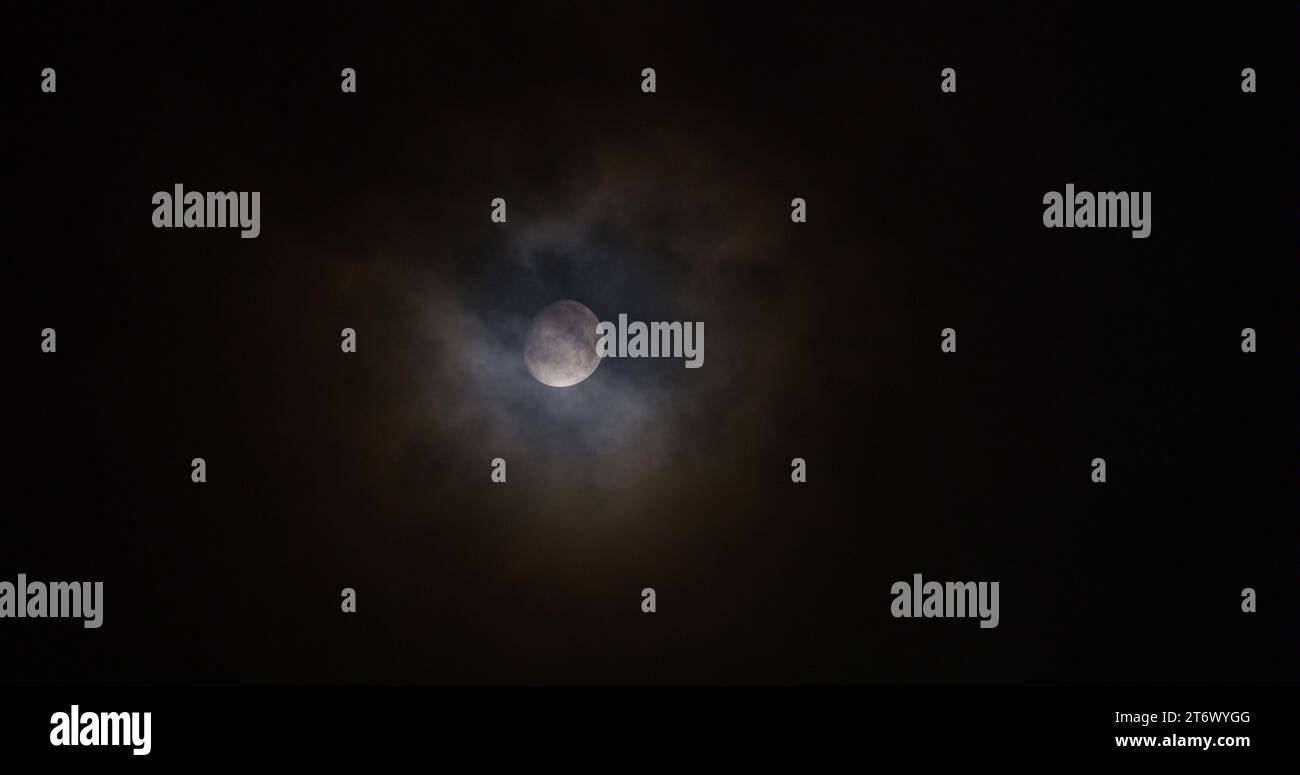 Ein verdunkelter Wolkenschleier zieht vor einem wachsenden Mond mit hypnotischer Wolkenbewegung vorbei. Stockfoto