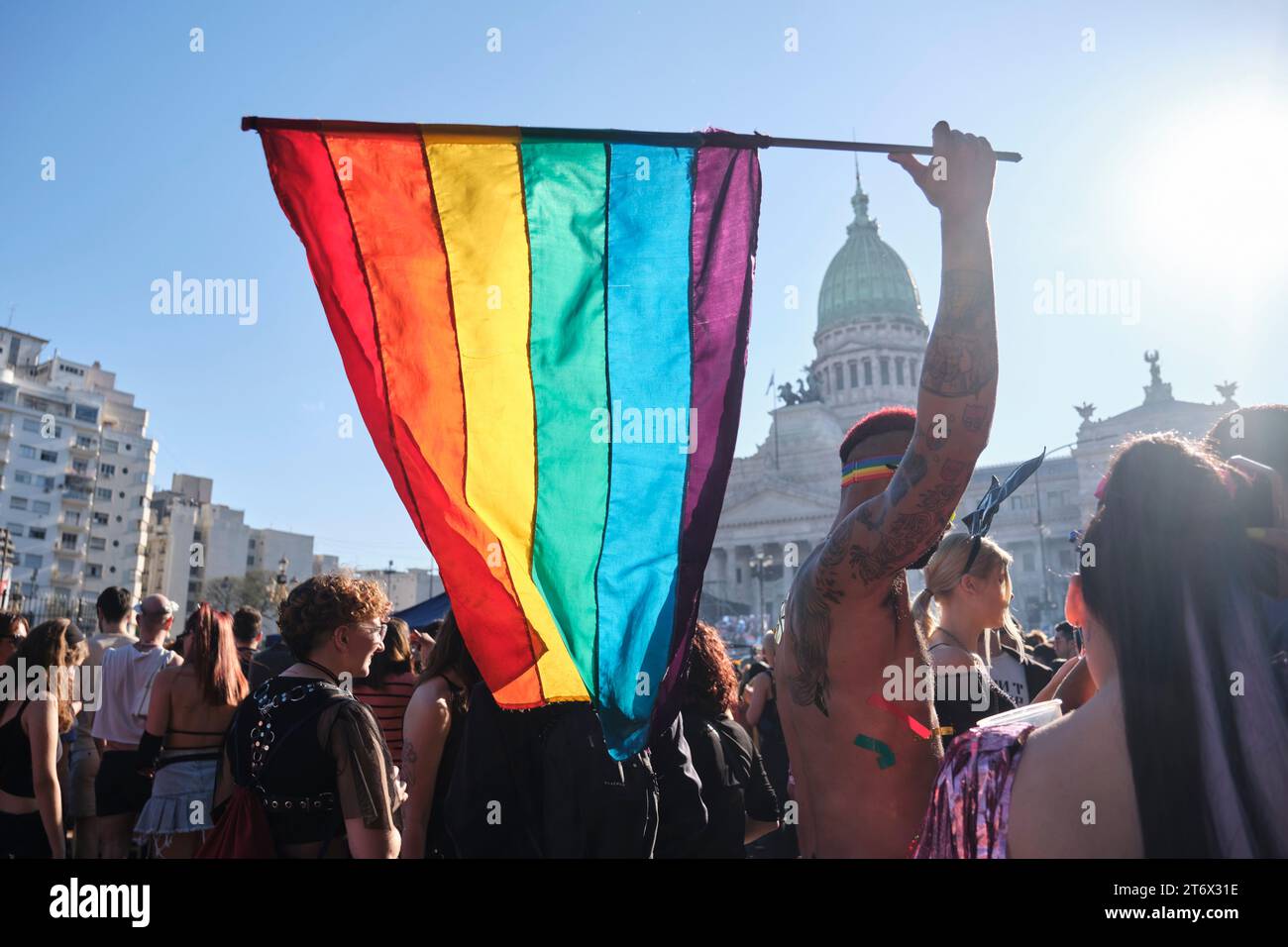 Buenos Aires, Argentinien; 4. November 2023: LGBT Pride Parade. Junger Mann, der vor dem Nationalkongress eine Regenbogenfahne hisst. Hintergrundbeleuchtete Bildmarkierung Stockfoto