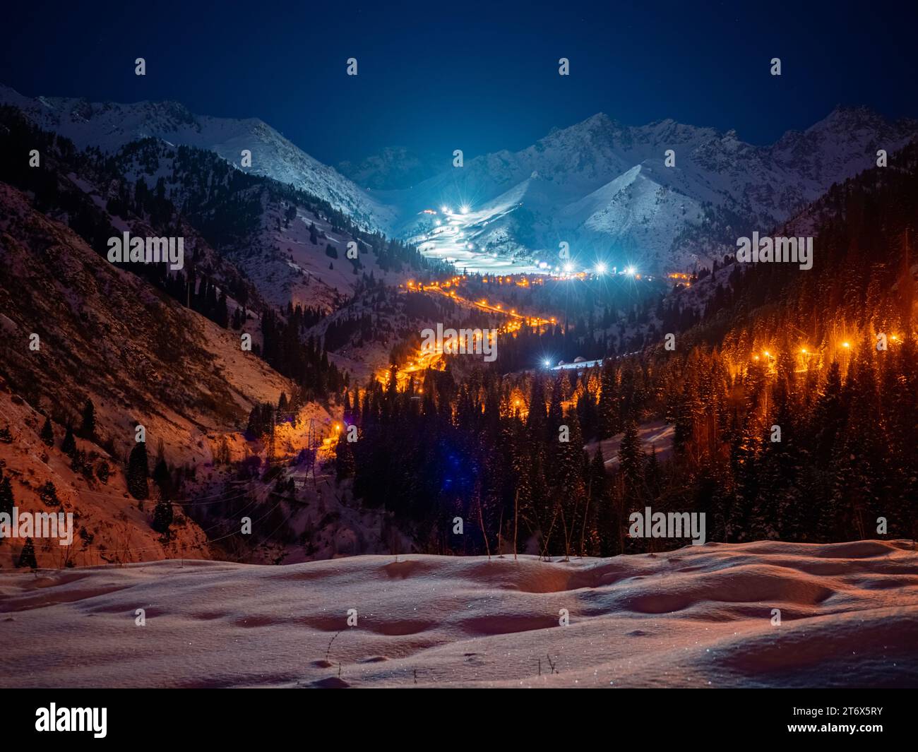 Nachtpanorama der beleuchteten Serpentinenstraße und des Chimbulak Skigebiets. Spätwinterabend hoch in den Bergen Stockfoto