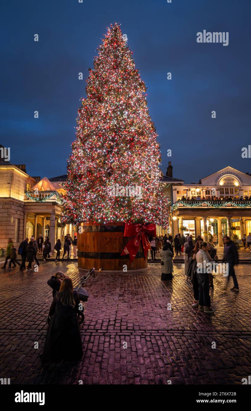 London, Großbritannien - 8. November 2023: Großer, geschmückter Weihnachtsbaum vor dem Covent Garden Market mit Leuten auf der Straße. Hochformat. Stockfoto