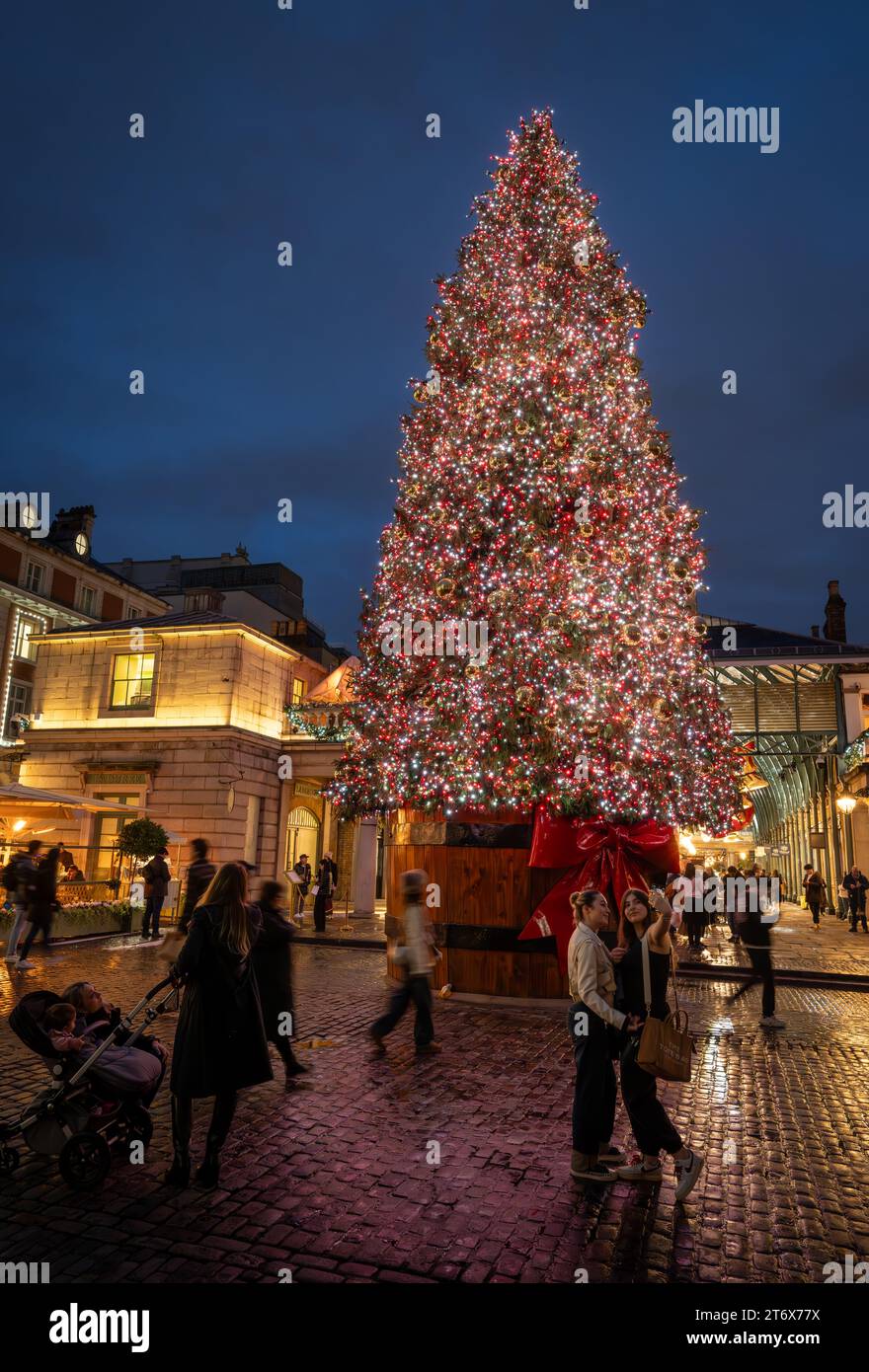 London, Großbritannien - 8. November 2023: Großer, geschmückter Weihnachtsbaum vor dem Covent Garden Market mit Leuten auf der Straße. Hochformat. Stockfoto