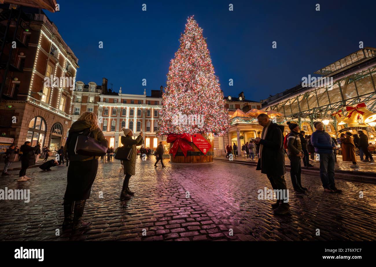 London, Großbritannien - 8. November 2023: Großer, geschmückter Weihnachtsbaum vor dem Covent Garden Market mit Leuten auf der Straße. Querformat mit niedrigem Winkel. Stockfoto