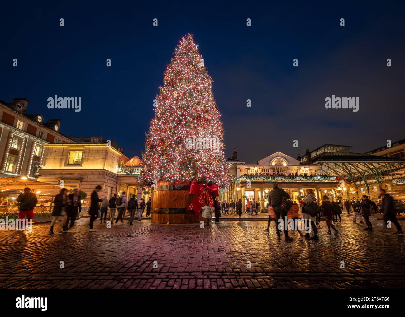 London, UK - 8. November 2023: Großer, dekorierter Weihnachtsbaum mit Covent Garden Market dahinter. Die Leute bewundern die Lichter auf dem Baum. Querformat. Stockfoto