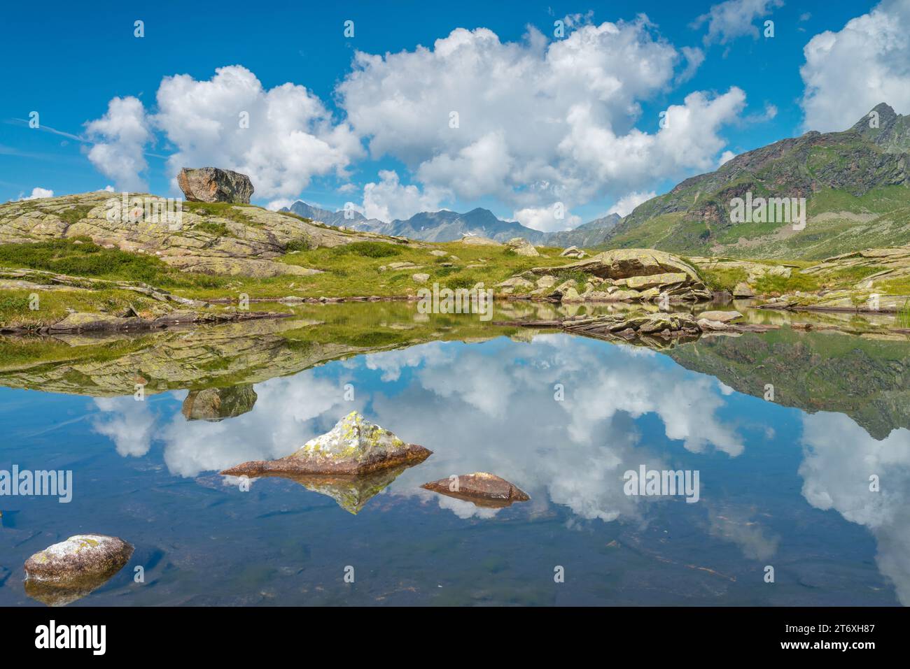 Himmel mit geschwollenen Wolken und großen Felsspiegeln auf einem kleinen alpinen Teich oben im Hochgebirgsland. Wasserreflexionen im kleinen See. Stockfoto