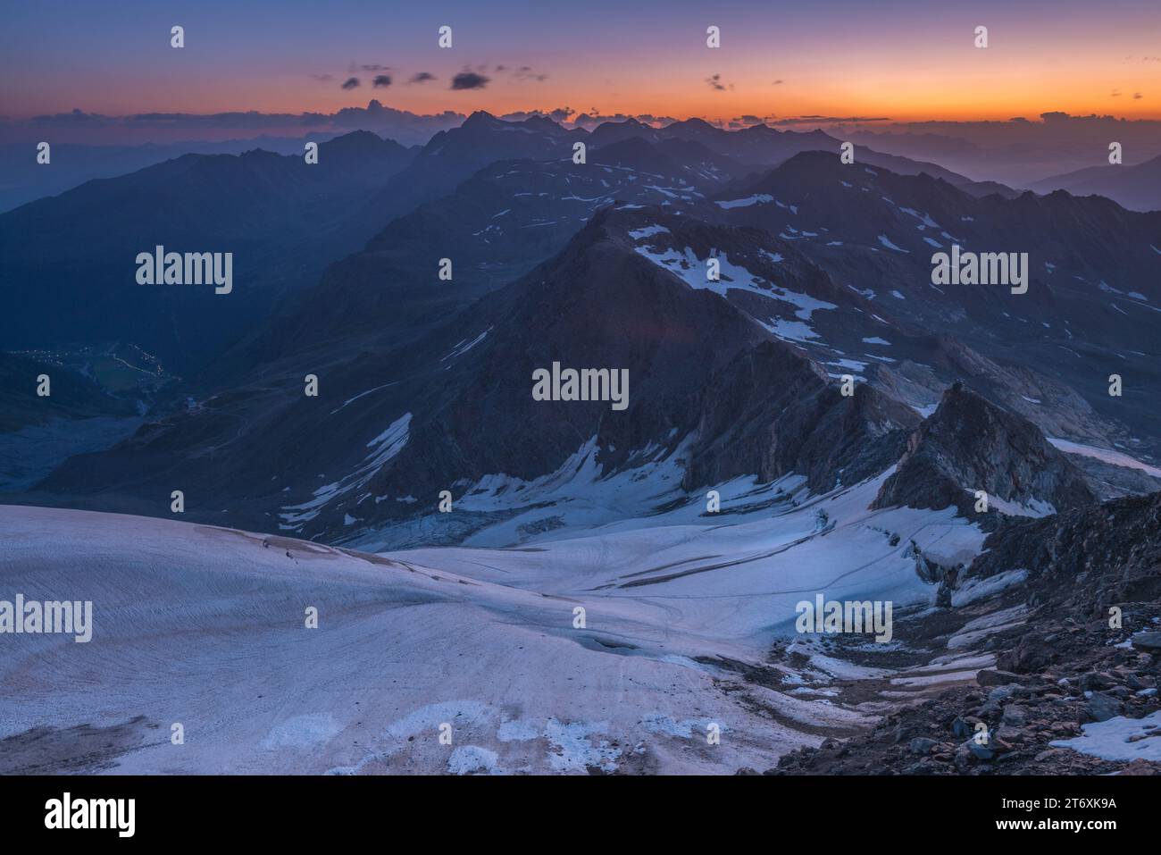 Alpiner Sonnenaufgang über kleinem Gletscher in den italienischen Alpen. Mehrere Berggipfel kurz vor Sonnenaufgang über dem Horizont. Stockfoto