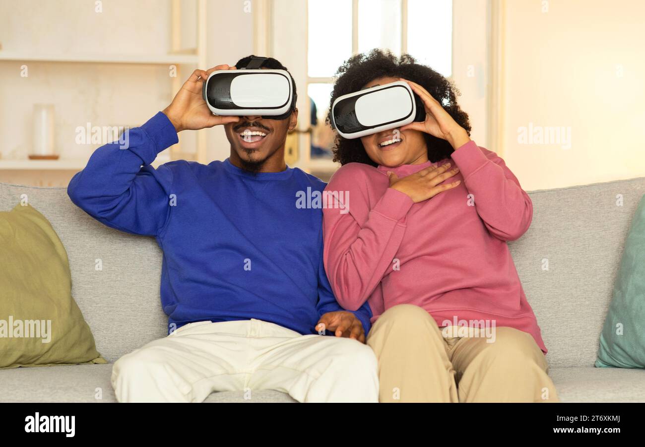 Afrikanische Ehepartner, die in Augmented Reality eintauchen und VR-Headsets im Innenbereich tragen Stockfoto