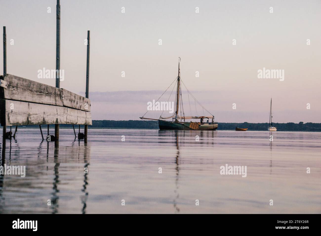 Altes Segelschiff neben einem Steg auf dem Wasser in der Dämmerung, Reflexion im Wasser Stockfoto