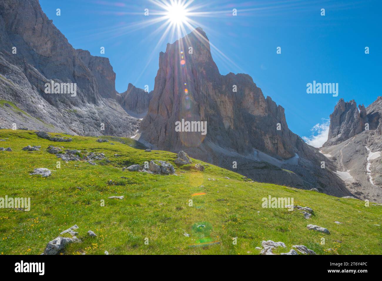 Direktes Sonnenlicht über dem Berggipfel in den italienischen Dolomiten. Alpine Landschaft mit grüner Sommerwiese, Sonnenstrahlen und blauem Himmel Stockfoto