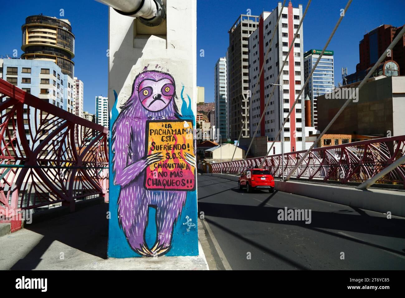 La Paz, Bolivien, 7. Juli 2022: Ein rotes Auto fährt an einem Wandgemälde auf einer Säule der Puente Gemelo/Zwillingsbrücke eines Faultieres vorbei, der gegen Chaqueos protestierte / Feuer begann, die tropischen Wälder der Chiquitania und Amazonas-Regionen des bolivianischen Tieflandes absichtlich zu beseitigen. Die Entwaldung ist insbesondere in Bolivien im letzten Jahrzehnt zu einem großen Problem geworden; 2022 wurde Bolivien von Global Forest Watch wegen Primärwaldverlusten an dritter Stelle der Welt gesetzt. Ein Großteil der Entwaldung ist die Politik der Regierung, die landwirtschaftliche Grenze des Landes auszuweiten, um Soja und Rinder für den Export nach China zu produzieren. Stockfoto