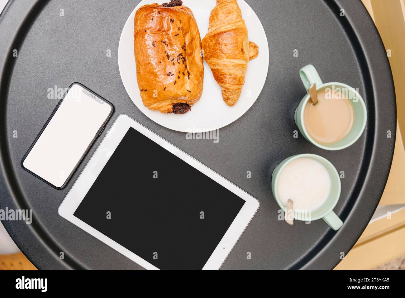 Croissants mit erhöhter Aussicht, Milchtee, elektronischer Gadgets-Tisch Stockfoto