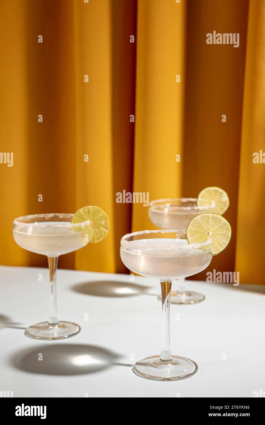 Glas-Margarita-Cocktail-Garnitur mit Limettentisch vor gelbem Vorhang Stockfoto