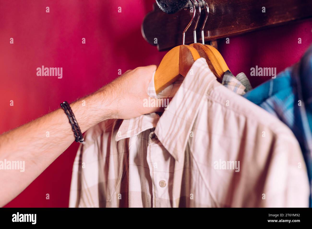 Die Hand des Mannes nimmt das Hemd des Kleiderbügels von der roten Wand Stockfoto
