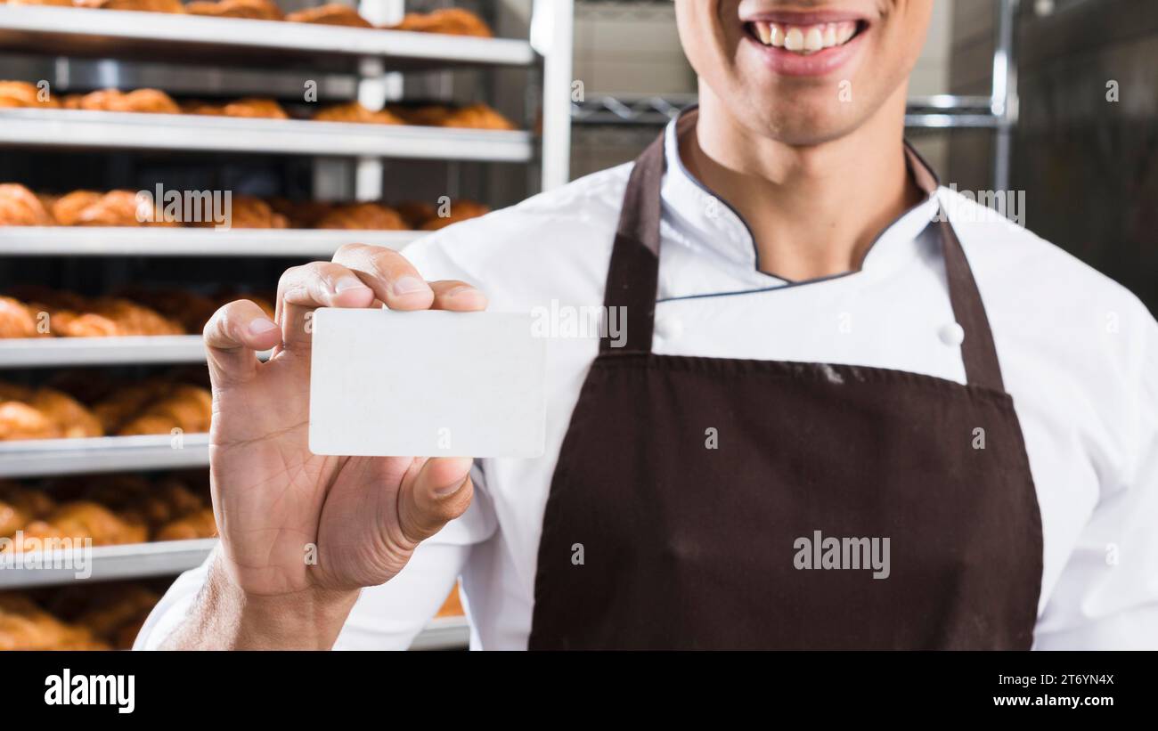 Ein lächelnder junger Bäcker hält eine weiße Visitenkarte Stockfoto