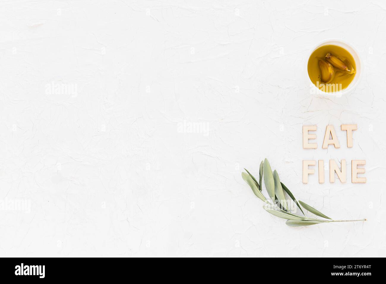 Essen Sie feinen Text mit Olivenzweig Knoblauchzehe Öl Schüssel mit weißem Hintergrund Stockfoto