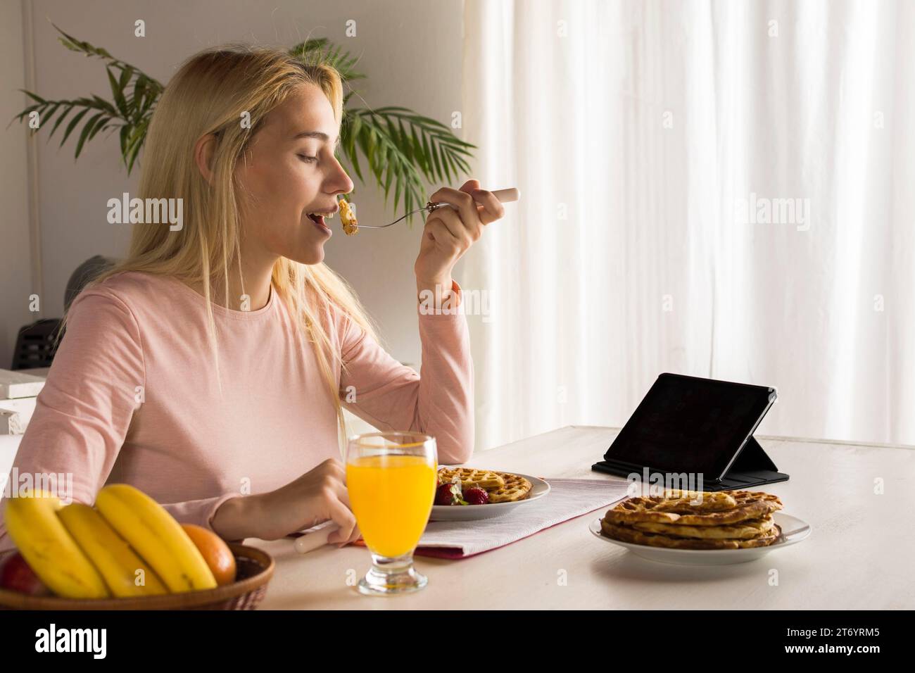Ein Mädchen isst Waffeln und beobachtet ein Tablet Stockfoto