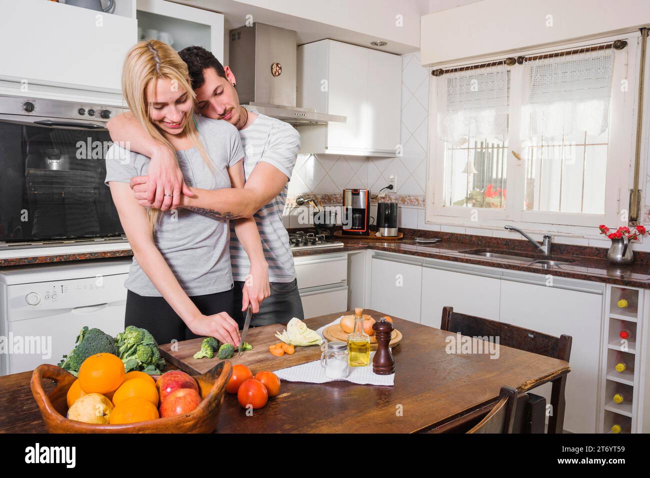 Ehemann lehnt seine Frau an die Schulter und schneidet Gemüse mit einem Messer Stockfoto