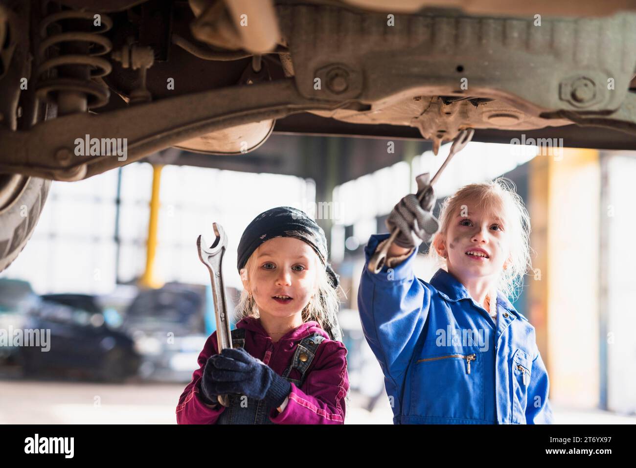 Zwei kleine Mädchen Overalls, die das Auto mit Schraubenschlüsseln reparieren Stockfoto