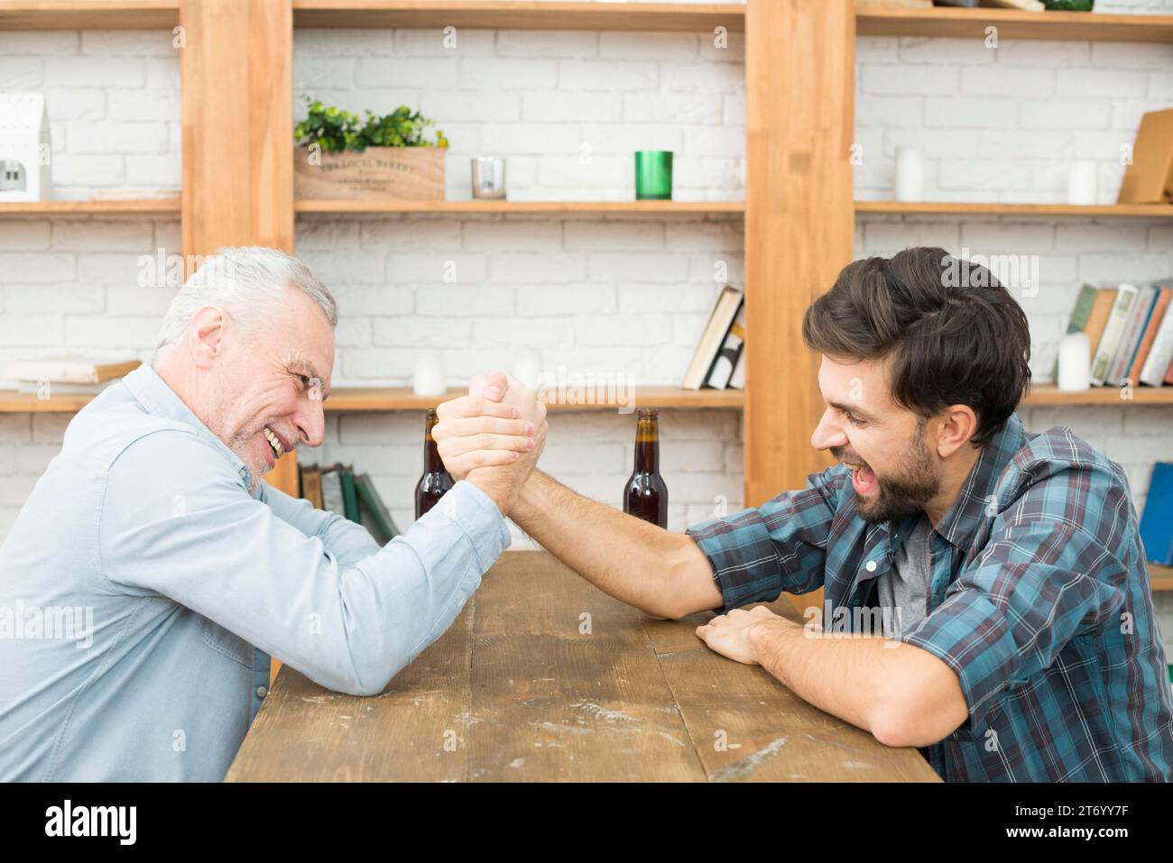 Alter Mann junger Mann mit Händen geklemmt Arm Wrestling Herausforderung Tisch Raum Stockfoto