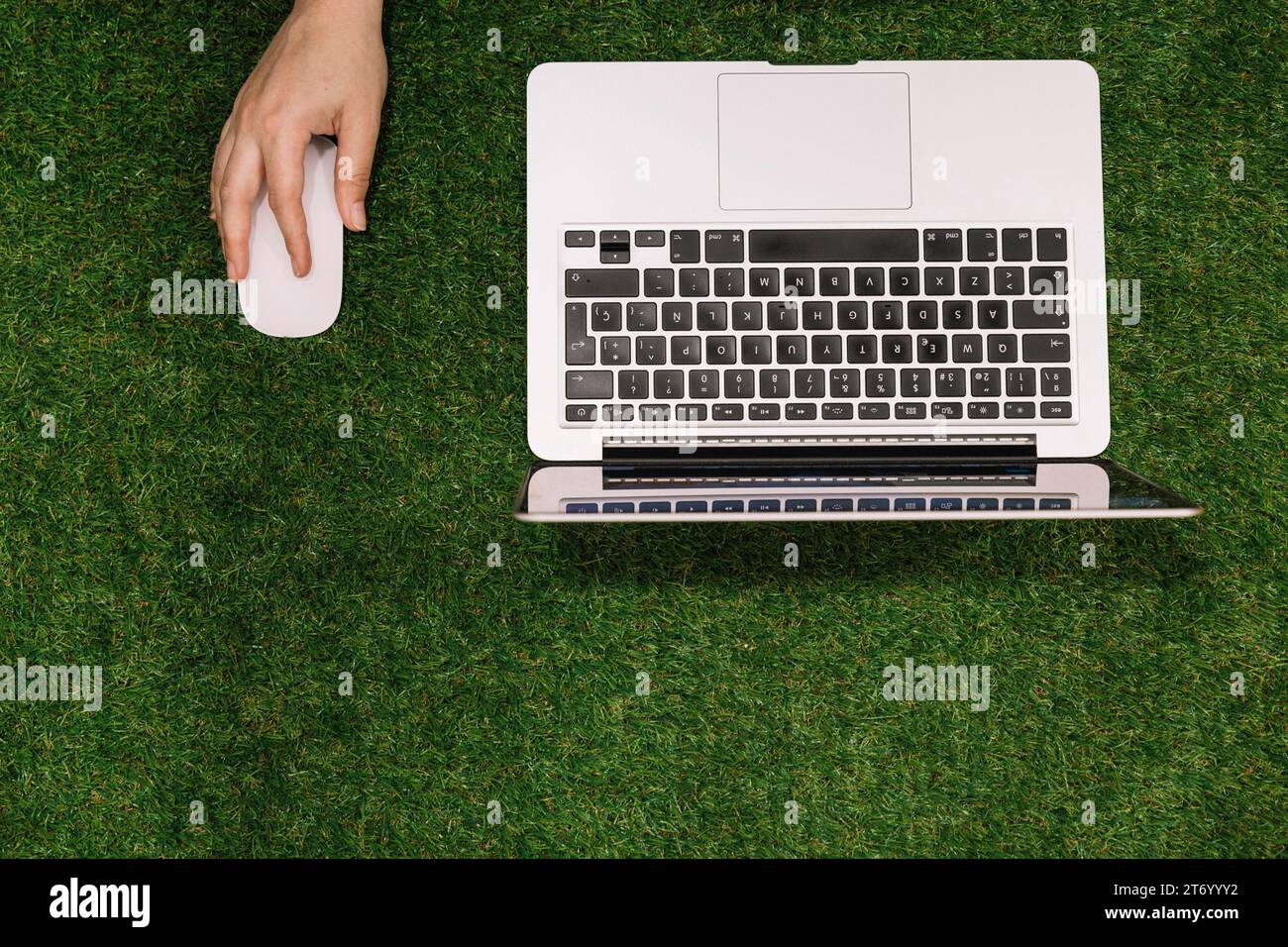 Nahaufnahme der Hand mit Maus und offenem Laptop mit falschem Gras im Hintergrund Stockfoto