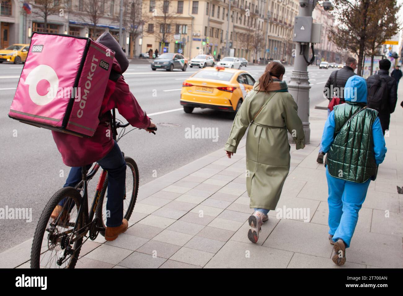 Ein Lieferer auf dem Fahrrad und regelmäßige Fußgänger teilen sich den Bürgersteig der Twerskaja Straße, Moskau, Russland Stockfoto
