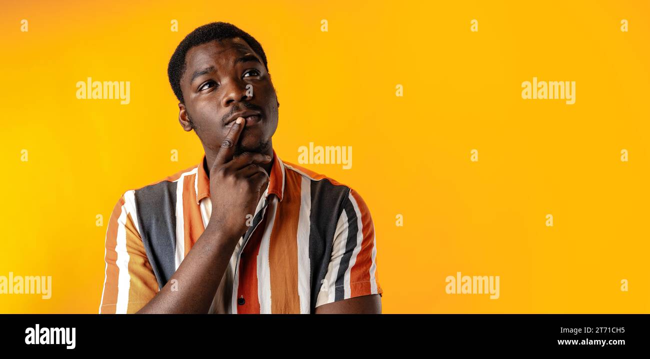 Junger afrikanischer Mann, der vor gelbem Hintergrund denkt Stockfoto