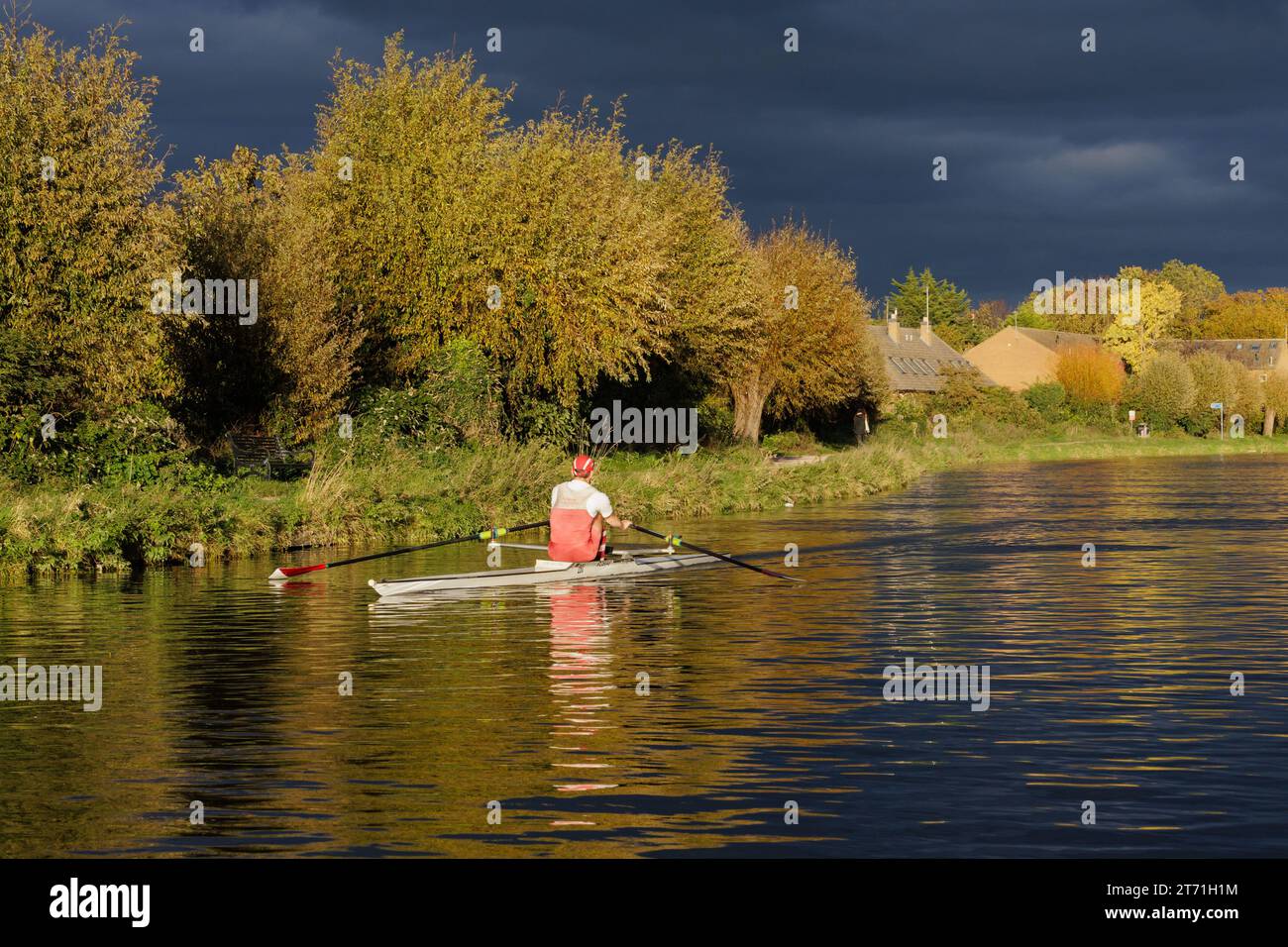 Ein Ruderer rudert auf dem Cambridge-Kanal mit dunklem bewölktem Himmel. Stockfoto