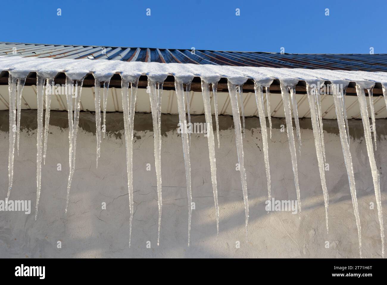 Scharfe Eiszapfen und geschmolzener Schnee hängen von den Dachtrassen. Wunderschöne, transparente Eiszapfen, die langsam über ein Dach gleiten. Stockfoto