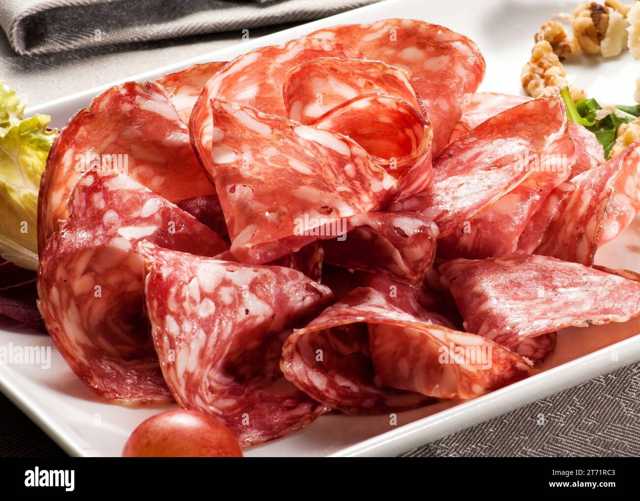 Im Restaurant werden köstliche Salamischeiben auf weißem Tablett mit Salatblättern serviert Stockfoto