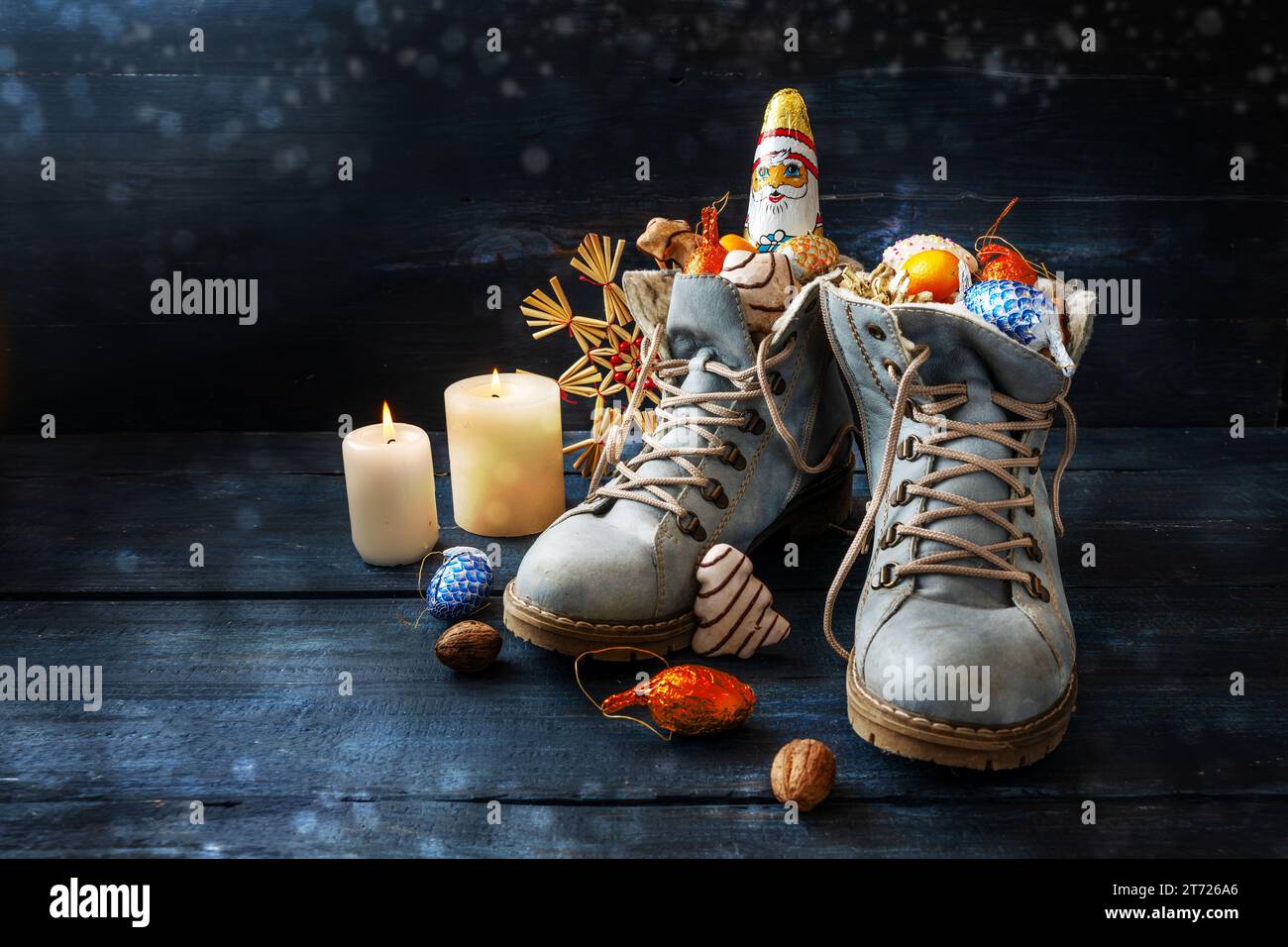 Tradition am deutschen Nikolaus Tag, was Nikolaus Tag bedeutet, Schuhe sind gefüllt mit Leckereien, hier Stiefel mit Süßigkeiten und Weihnachtsdekoration auf dunkelblauem Holz Stockfoto
