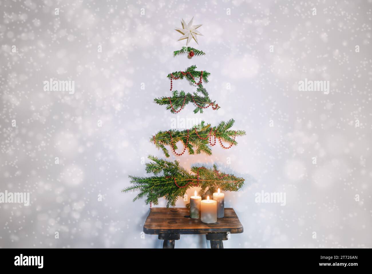 Weihnachtsbaumalternative, immergrüne Zweige mit Dekoration, die an der Wand über einem rustikalen Holzhocker mit Kerzen hängen, nachhaltige Feiertage Agave Stockfoto