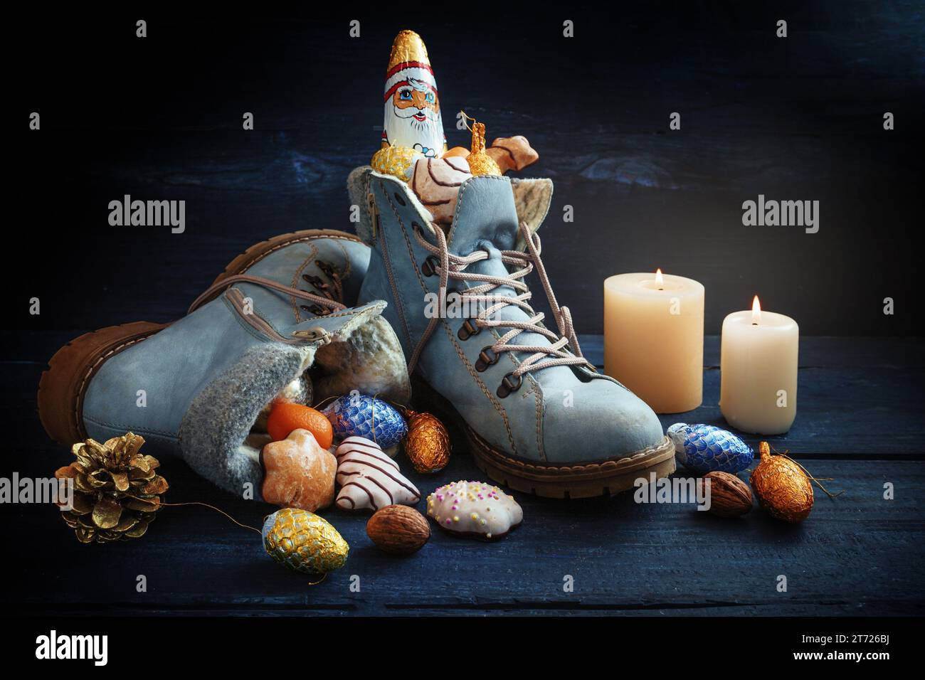 Blaue Stiefel gefüllt mit Süßigkeiten, Weihnachtsdekoration und ein Schokoladen-Weihnachtsmann auf dunklem Holz mit Kerzen, Tradition auf dem deutschen Nikolaus-Tag, was Nikolaus bedeutet Stockfoto