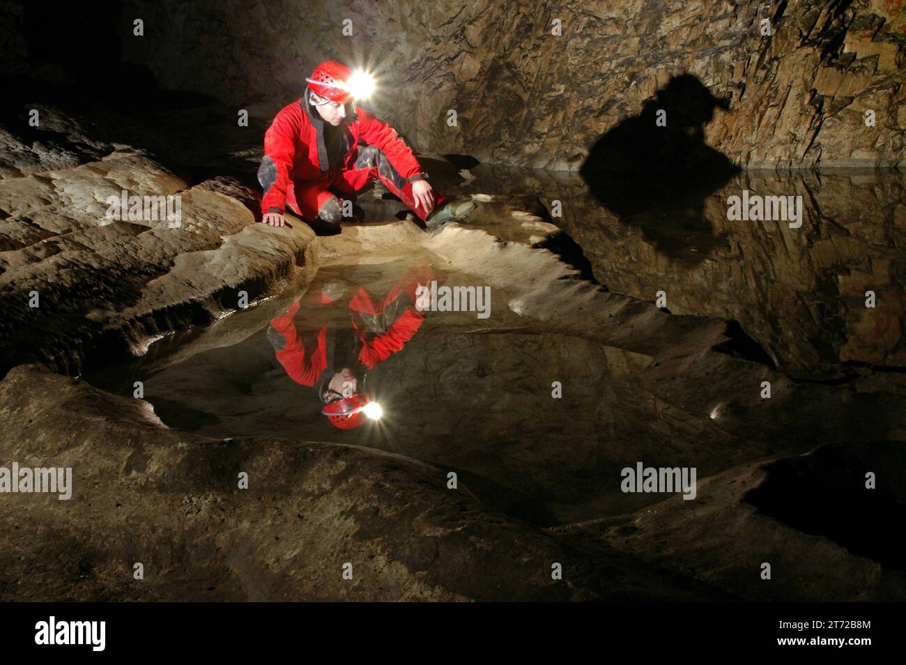 Reflexion eines Spelunkers in einem Höhlenwasserbecken. Carbid-Acetylen-Gaslampe am Helm, die den Boden beleuchtet Stockfoto