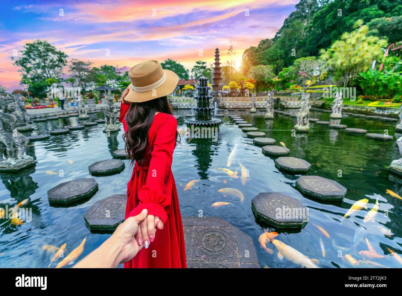 Touristen, die die Hand des Mannes halten und ihn zum Tirta Gangga Water Palace in Bali, Indonesien, führen. Stockfoto