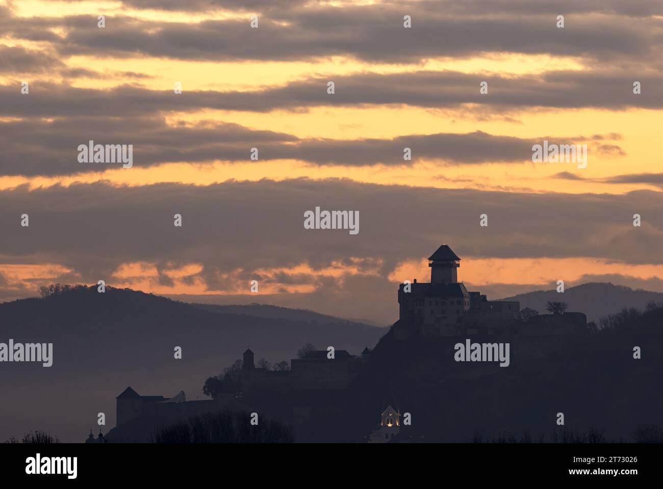 Schlosssilhouette bei Sonnenaufgang im Morgennebel. Auf einem Felsen stehen. Mit einem wunderschönen bunten, bewölkten Himmel. Herbstlandschaft. Trencin, Slowakei Stockfoto