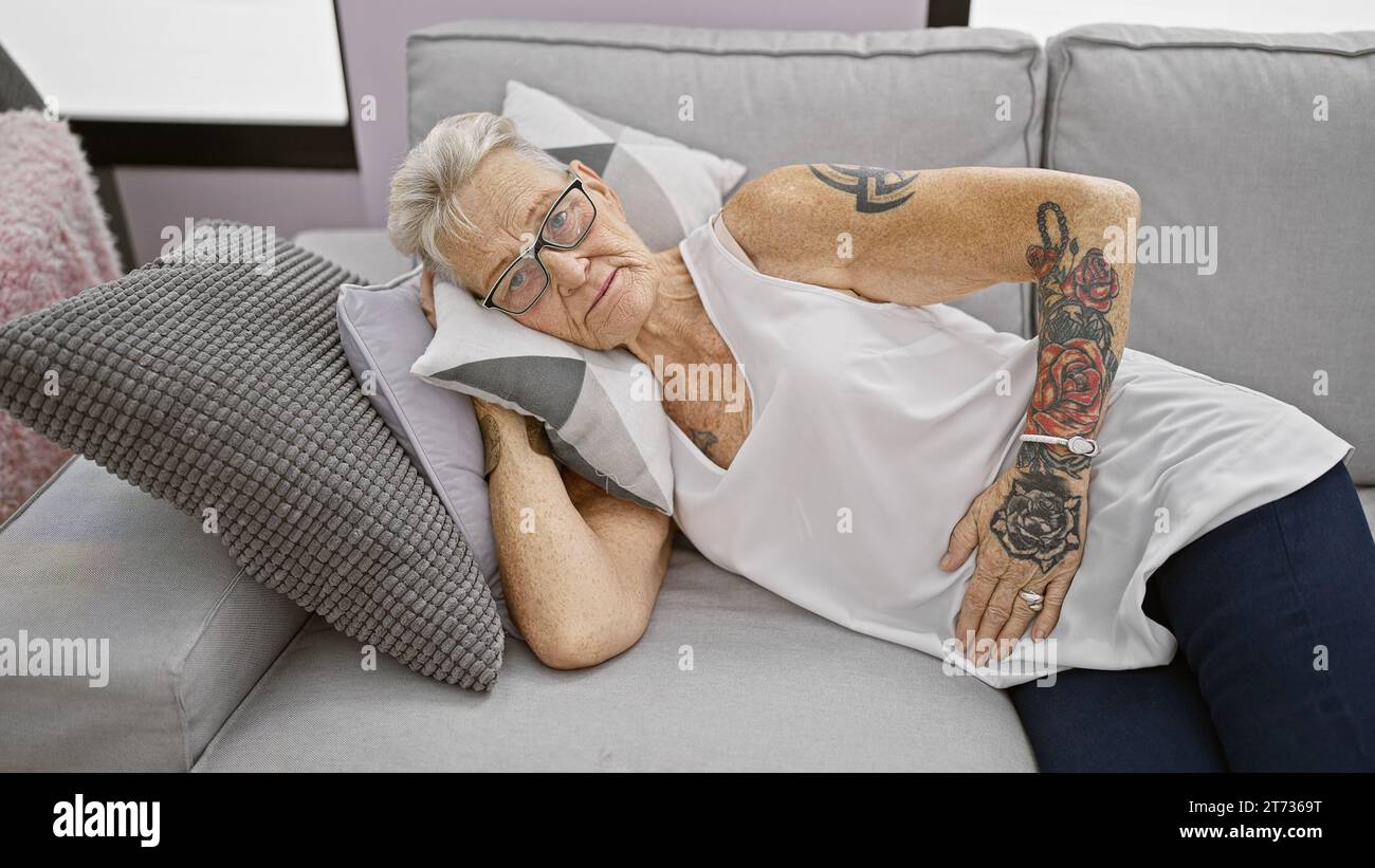 Unglückliche grauhaarige ältere Frau, die unter starken Magenschmerzen leidet, während sie sich zu Hause auf dem Sofa ausruht Stockfoto