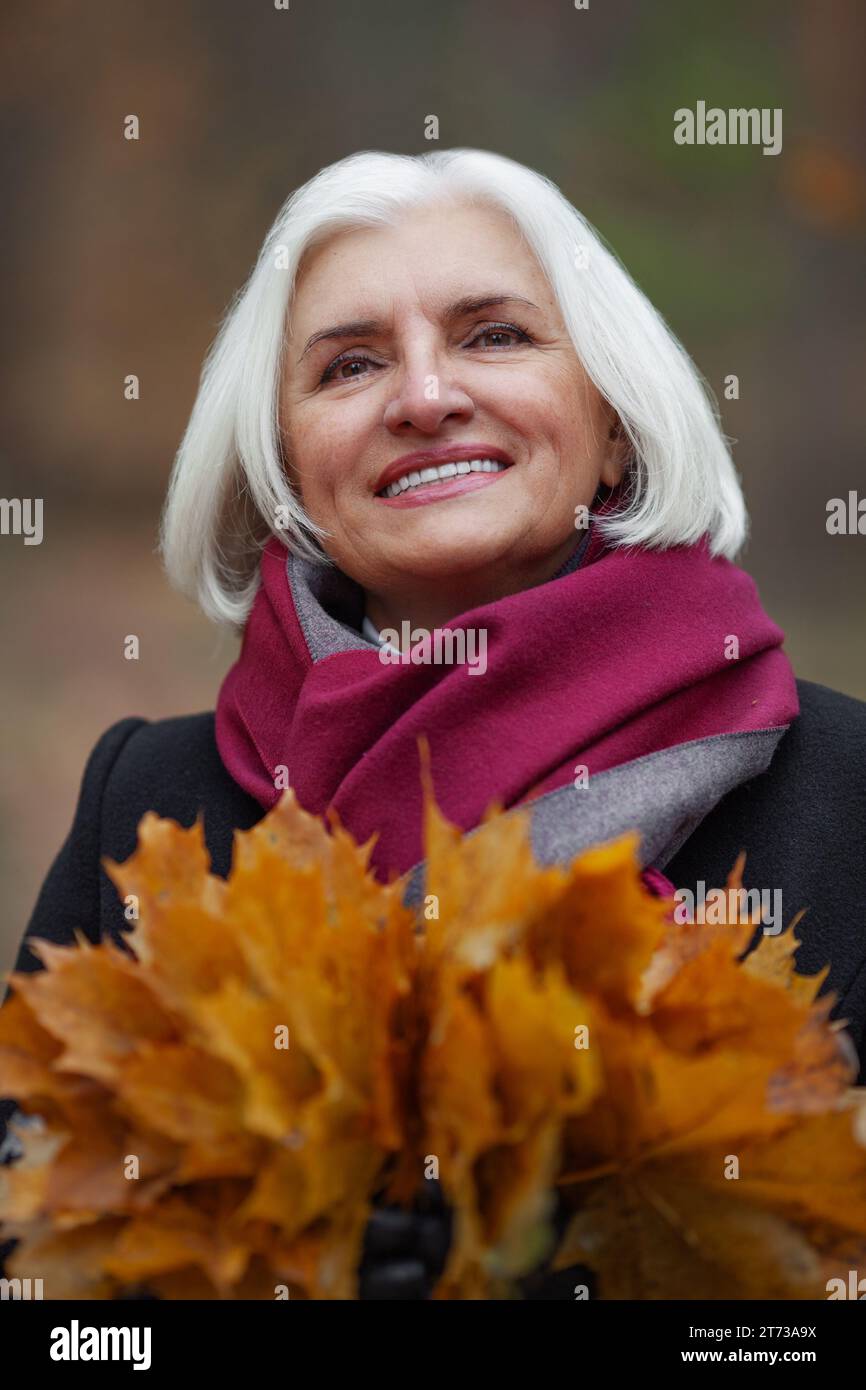 Nahaufnahme kaukasische fröhliche grauhaarige alte Frau mit Herbstlaub, die draußen lächelt. Glückliche reife Frau Porträt einer älteren, schönen Dame, die Li genießt Stockfoto