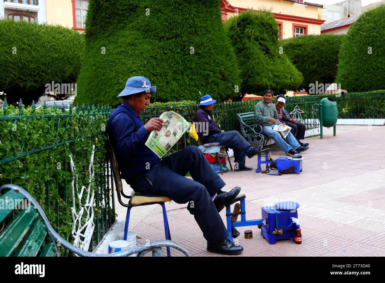 Ein Schuhputzer liest eine Zeitung, während er auf den Plaza de Armas in Puno, Peru, wartet Stockfoto