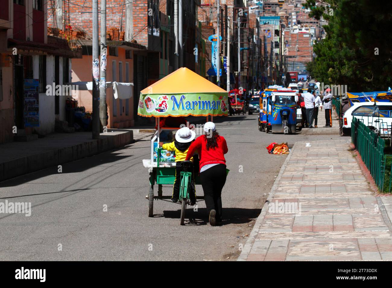 Eine Frau und ihre Tochter schieben einen Dreiradwagen mit Ceviche (roher, marinierter Fisch, ein berühmtes typisches peruanisches Gericht) entlang einer Straße in Puno, Peru Stockfoto