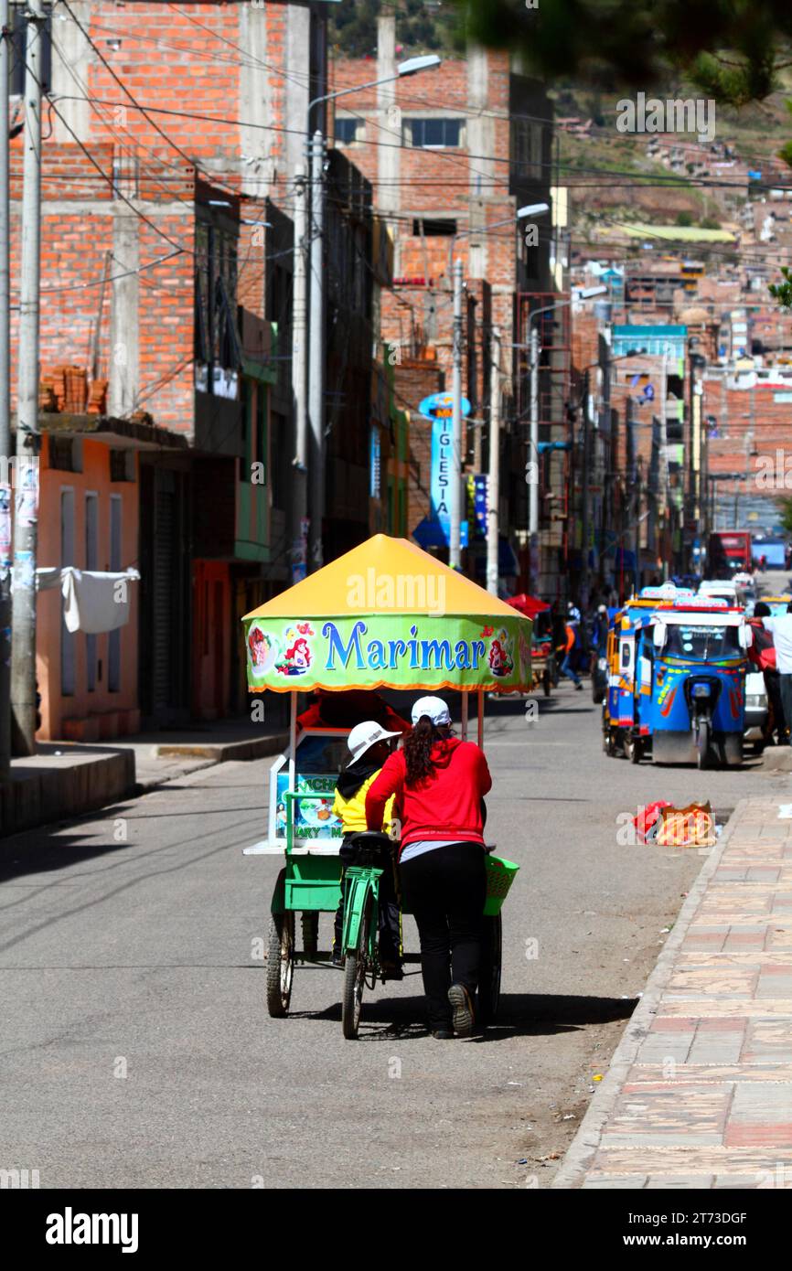 Eine Frau und ihre Tochter schieben einen Dreiradwagen mit Ceviche (roher, marinierter Fisch, ein berühmtes typisches peruanisches Gericht) entlang einer Straße in Puno, Peru Stockfoto